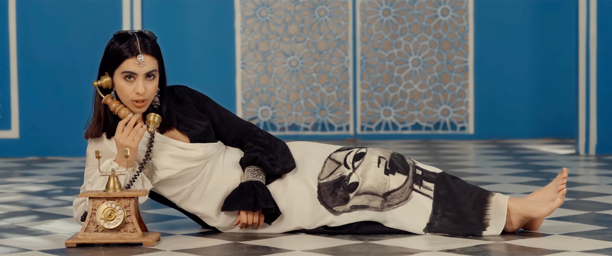 Ranjani reclining on a checkerboard floor holding a vintage brass telephone