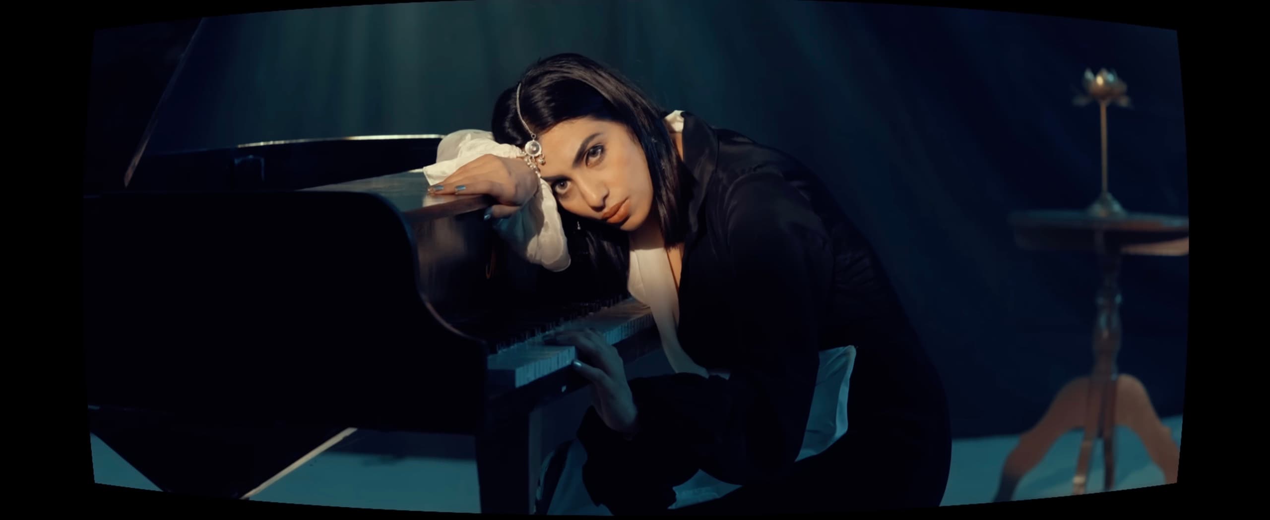 Ranjani in black silk at a grand piano under a teal spotlight
